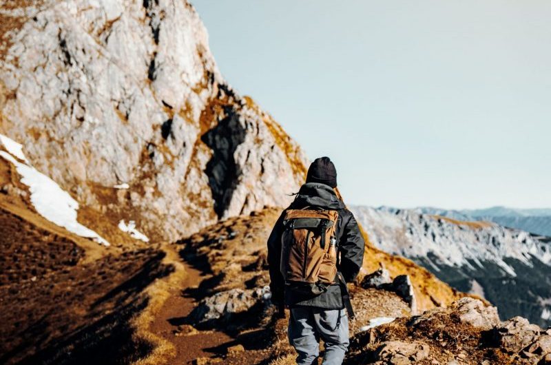 man in brown jacket and gray pants standing on brown rocky mountain during daytime