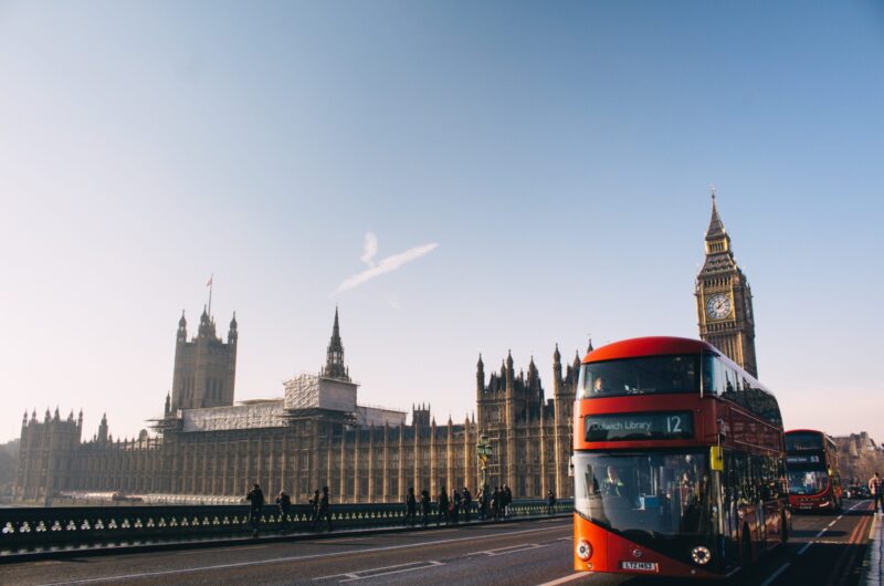 red double-decker bus passing Palace of Westminster, London during daytime